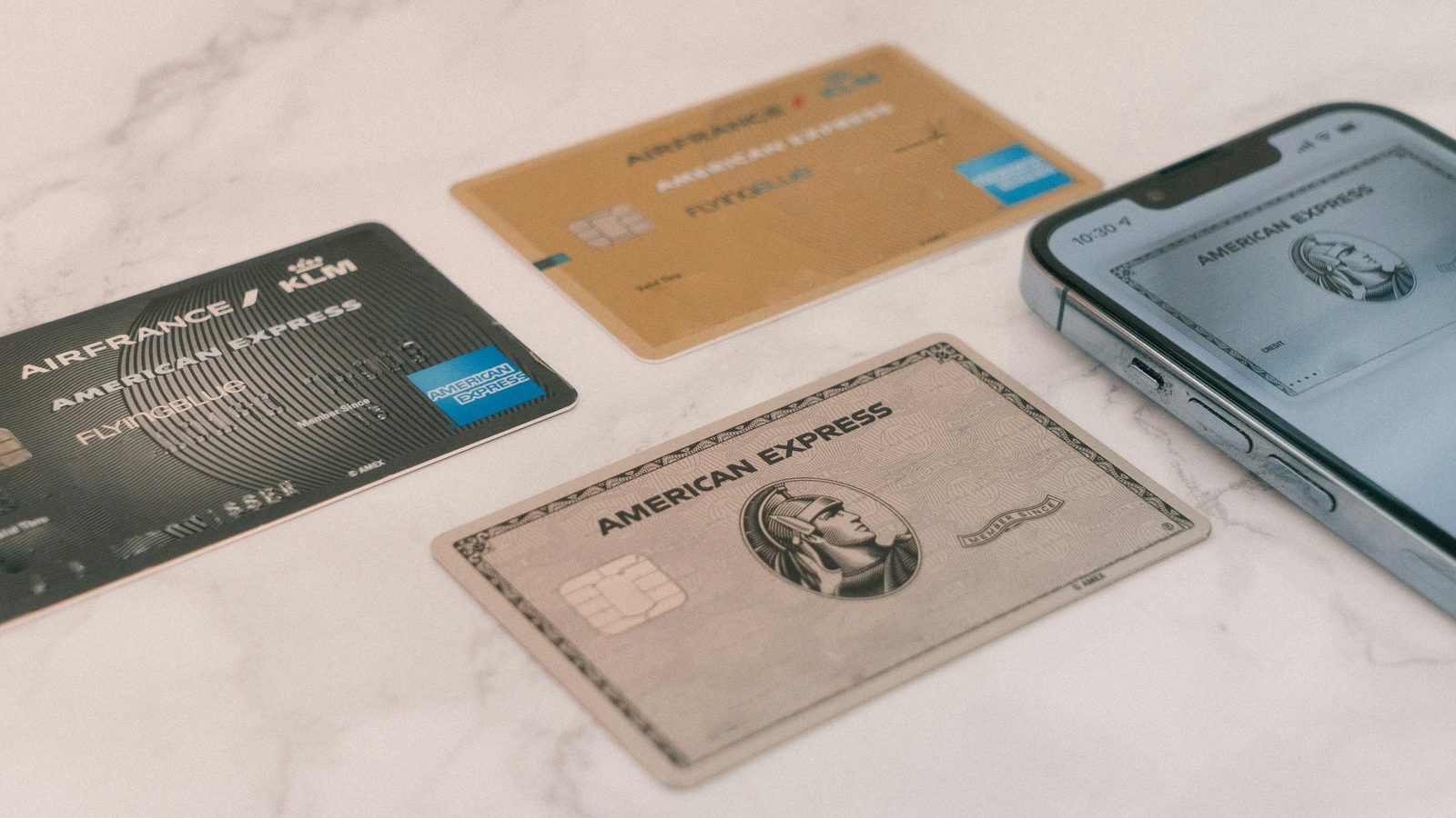 Three credit cards laid out on a marble surface beside a phone showing a card in a digital wallet