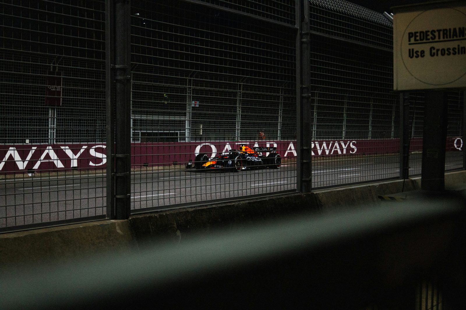 A Red Bull Formula 1 car on a floodlit street circuit at night, seen through catch fencing
