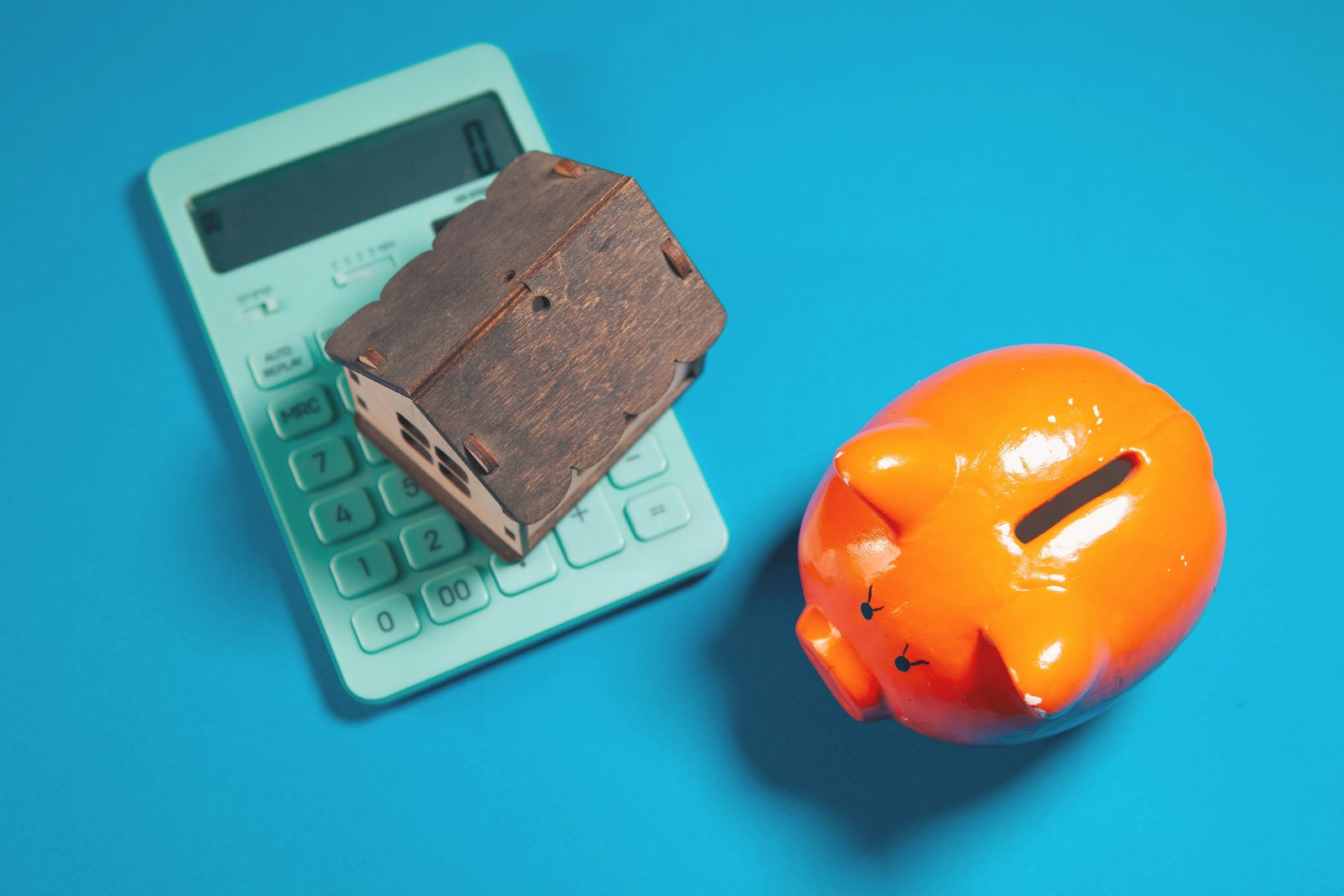 A model house resting on a calculator beside an orange piggy bank