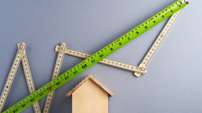 Folding rulers and a tape measure above a small wooden house