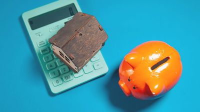 A model house on a calculator next to a piggy bank